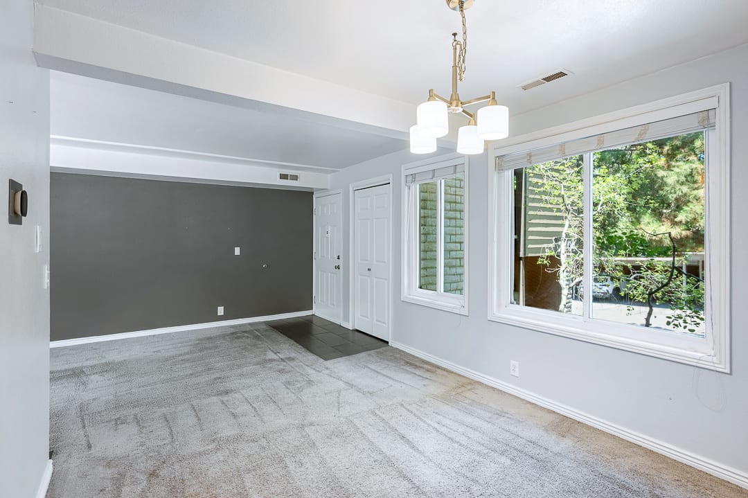 Living space featuring a neutral color palette, two large windows with roller blinds, and a brass-tone chandelier