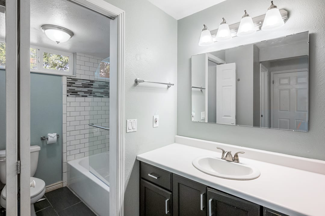 Bathroom featuring a dark wood-finish vanity with a white countertop, a rectangular mirror, and a four-light fixture