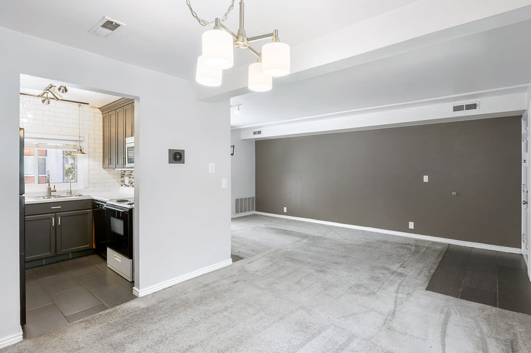 Open-concept living space featuring a modern chandelier, light gray carpeting, and a contrasting accent wall