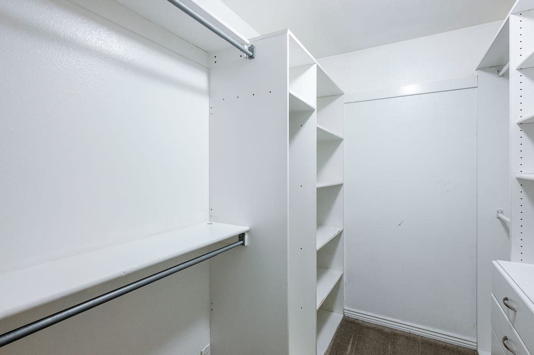 Walk-in closet featuring white built-in shelving, hanging rods, and a multi-drawer unit