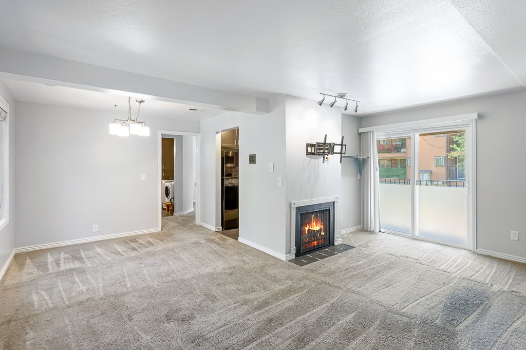 Spacious living area featuring a fireplace with black surround, track lighting, sliding glass door access to an exterior balcony, and a dedicated dining area with a chandelier
