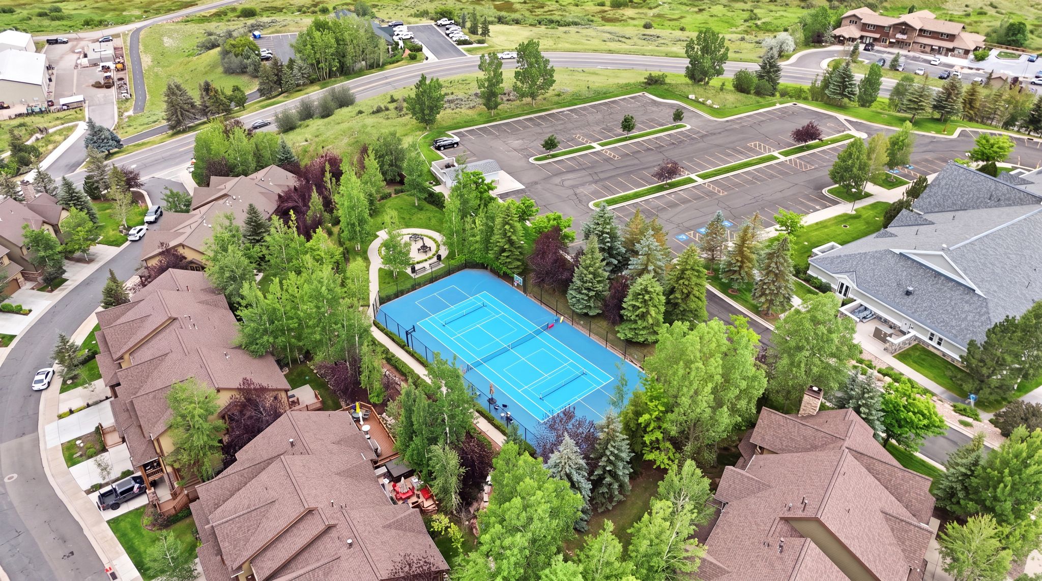 Tennis court surrounded by mature trees, adjacent to residential structures
