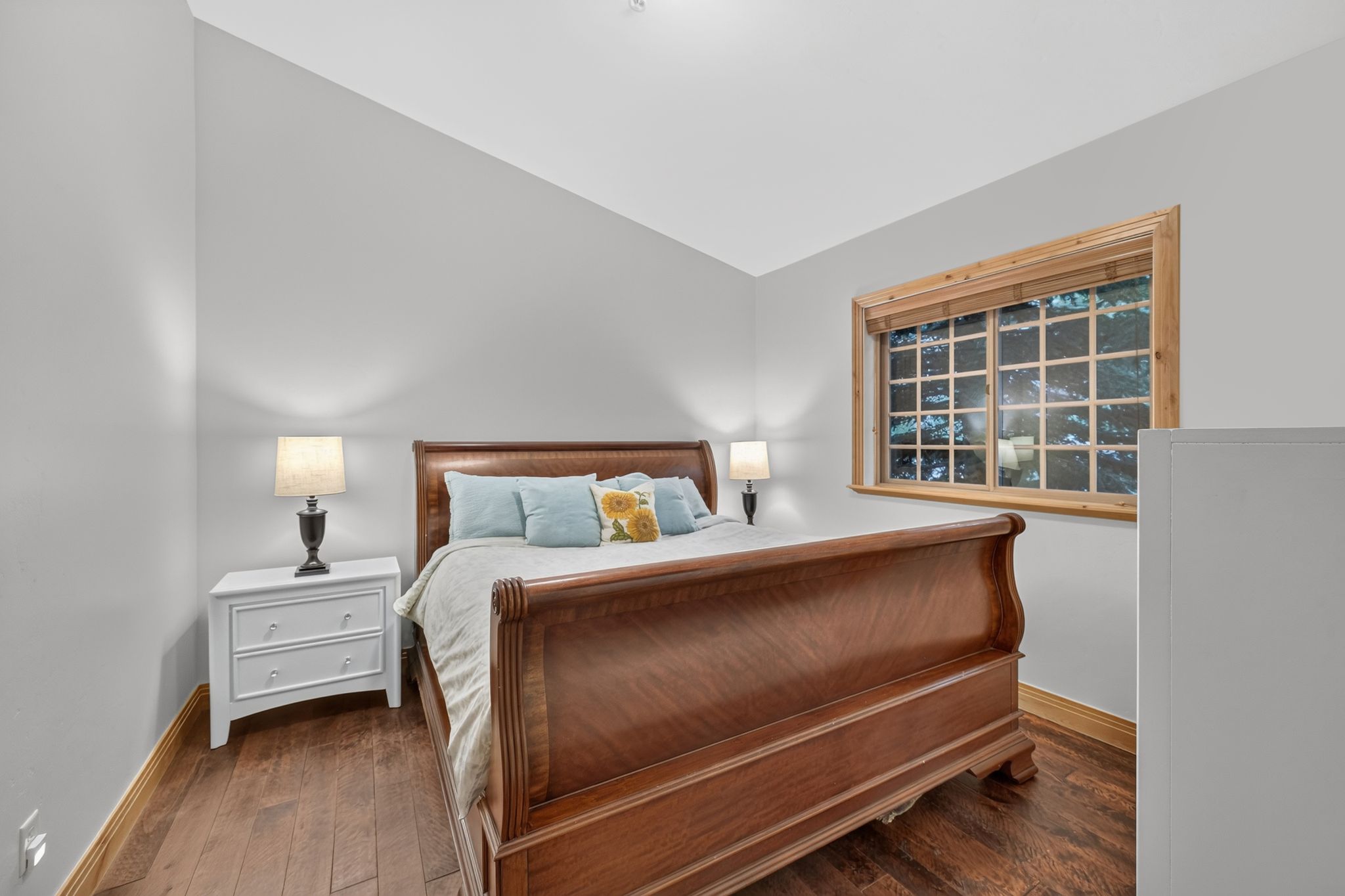 Spacious room featuring wood-finish flooring, a multi-pane window with natural wood trim, and light gray walls