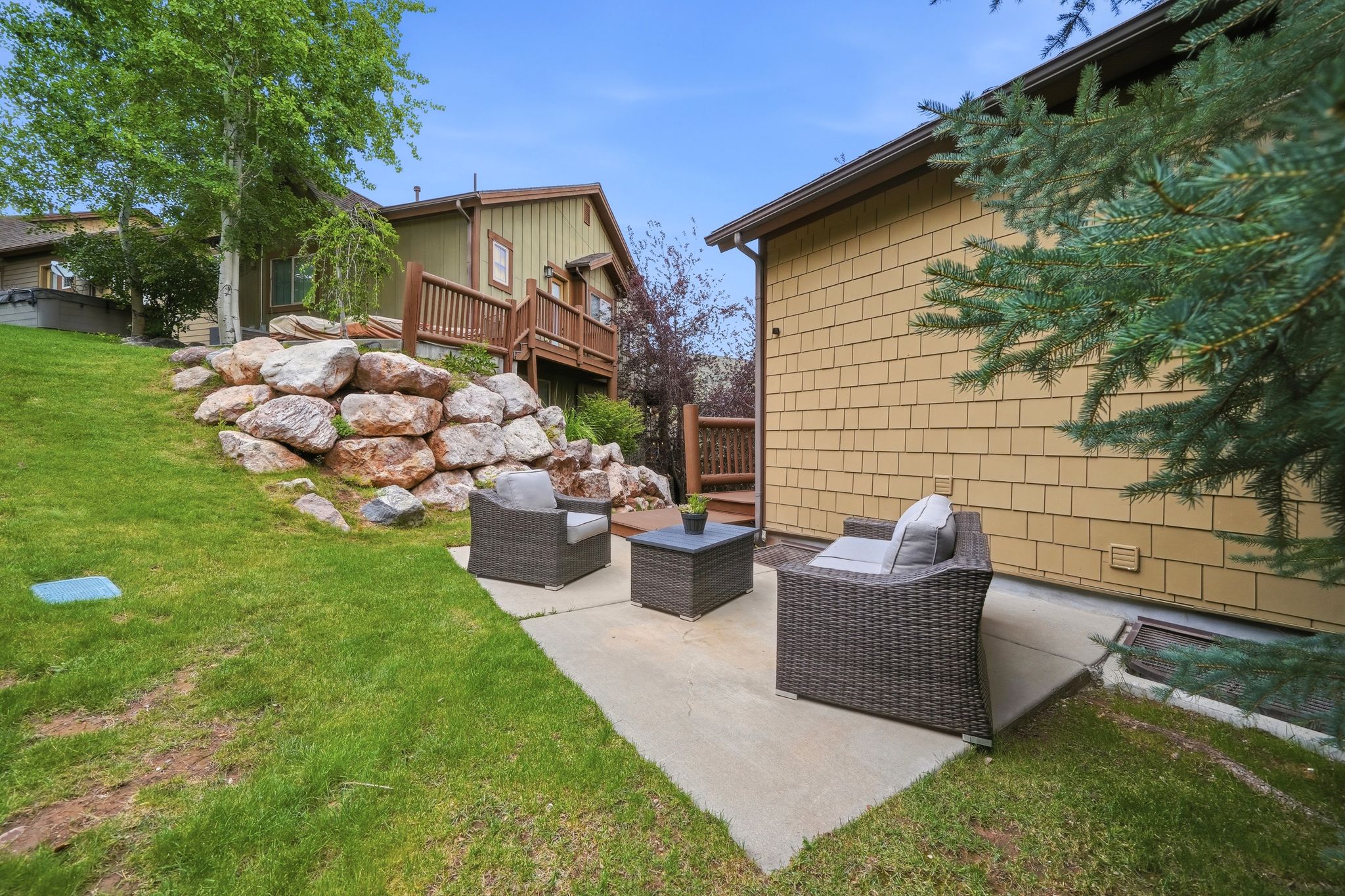 Concrete patio with a rock retaining wall and sloped lawn