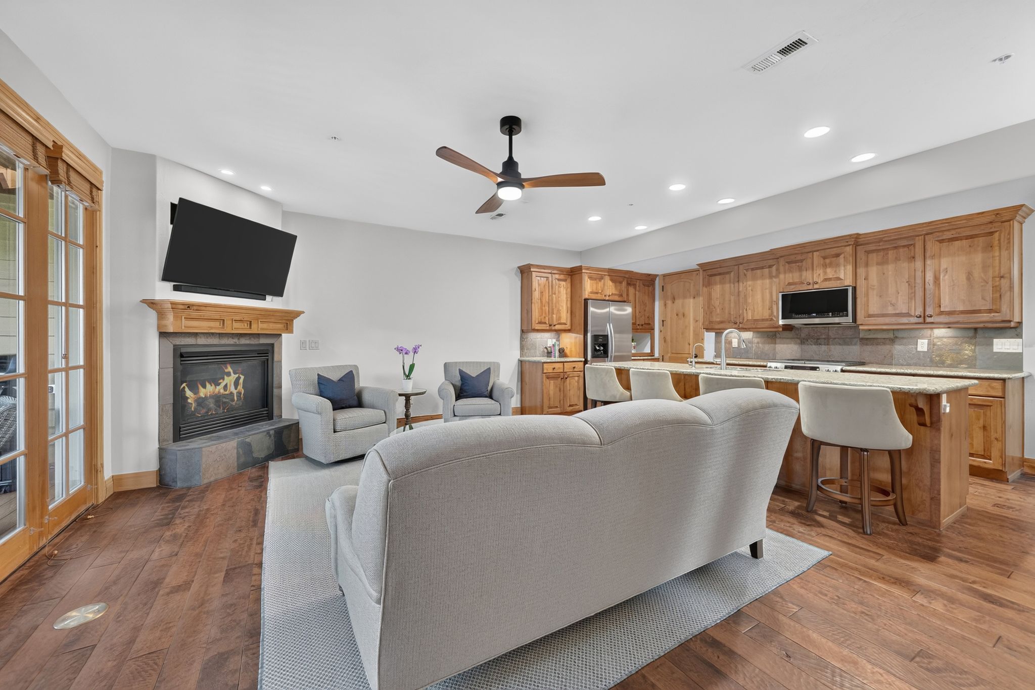 Open-concept living space featuring wood-finish flooring, a stone-surround fireplace with a wood mantel, a ceiling fan, and recessed lighting