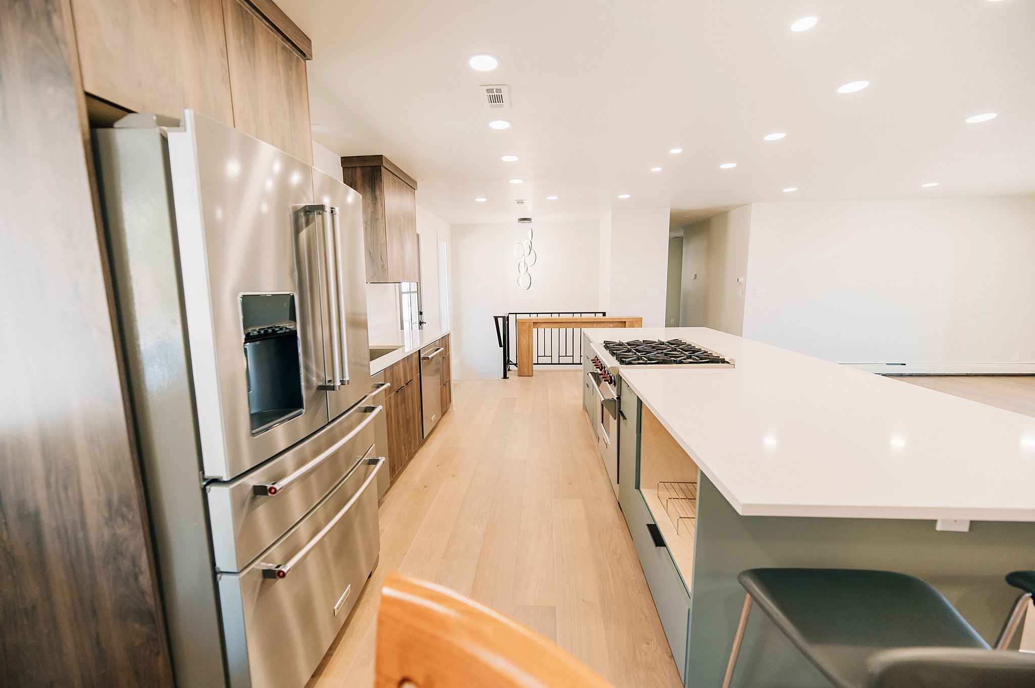 Modern kitchen featuring a large center island with integrated gas cooktop, light-toned wood-finish flooring, recessed lighting, stainless steel appliances, and contrasting dark wood-finish cabinetry