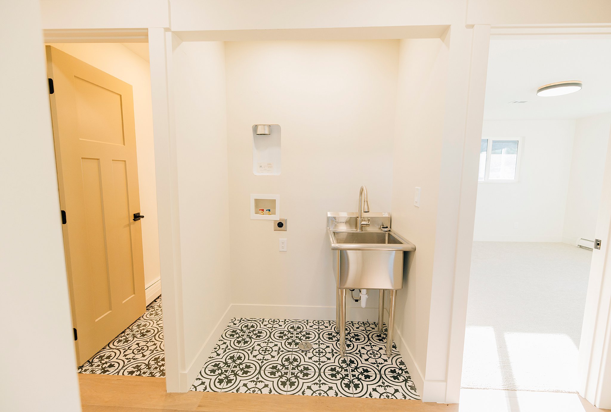 Dedicated laundry area featuring patterned floor tiles, a stainless steel utility sink with a brushed metal faucet, and accessible appliance connections