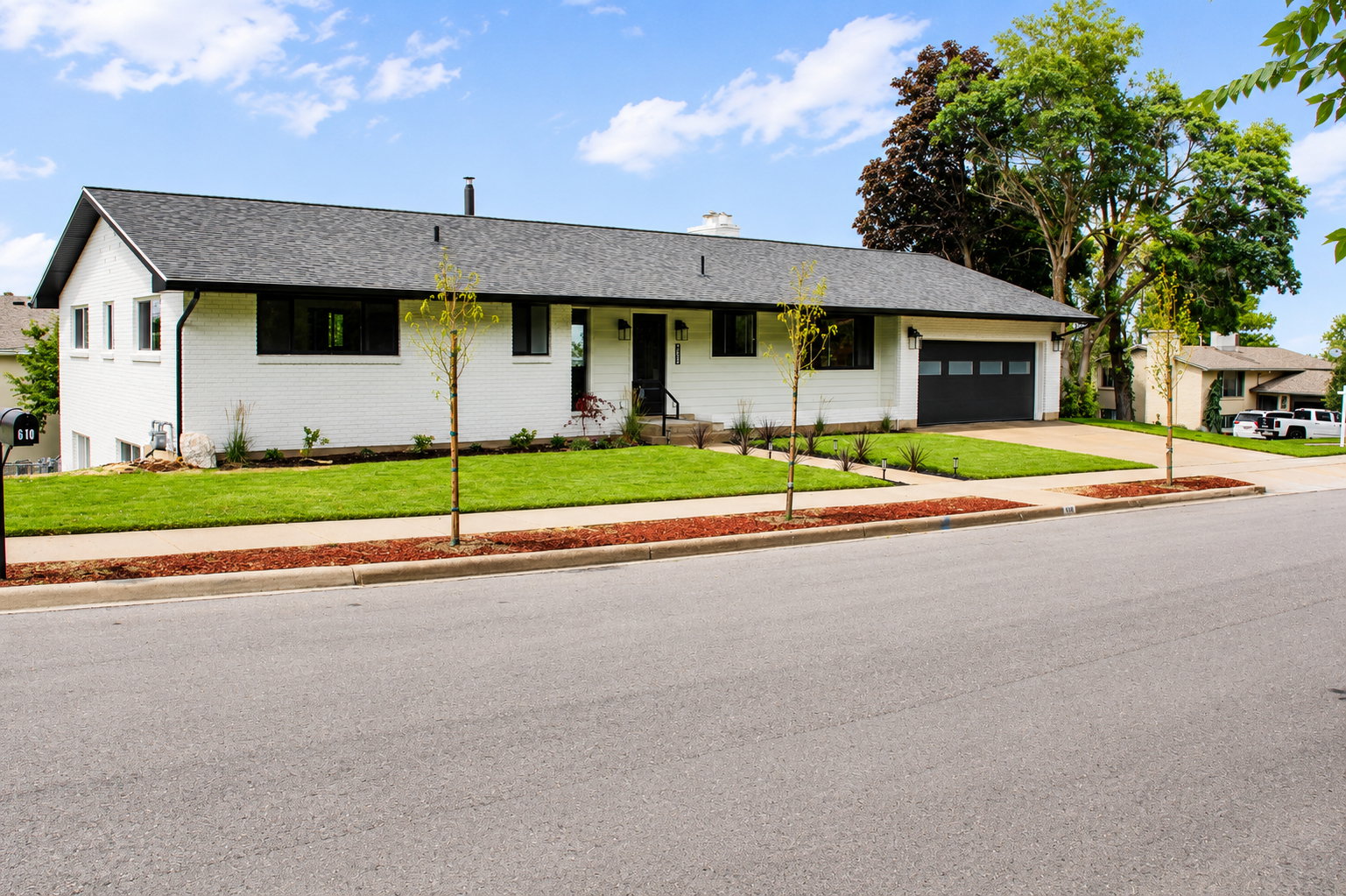 Contemporary ranch-style home featuring white brick exterior, black-framed windows, dark gray garage door, and a contrasting black roof
