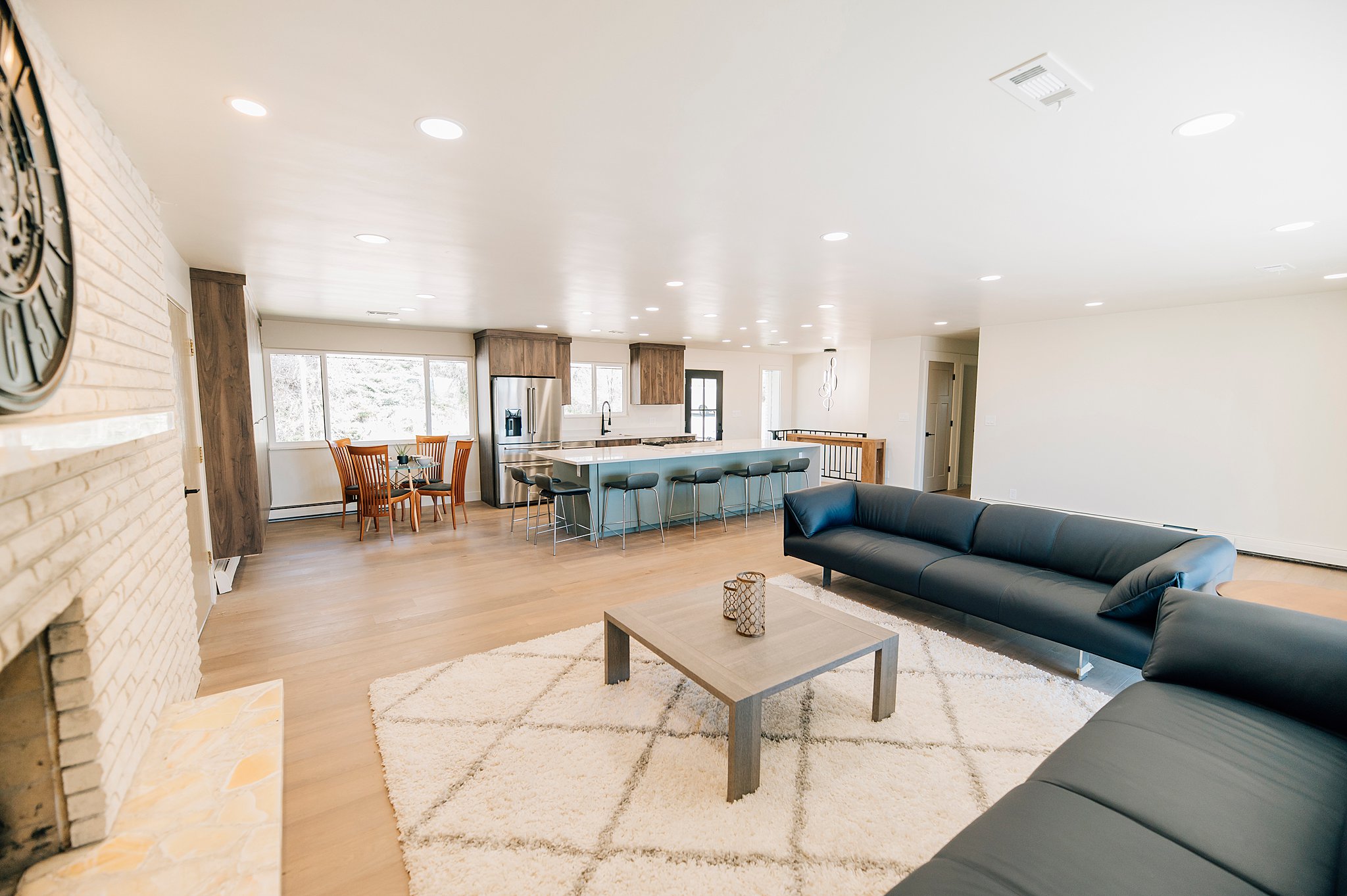 Open-concept living space featuring wood-finish flooring, a white brick fireplace, recessed lighting, and a kitchen with an island and stainless steel appliances