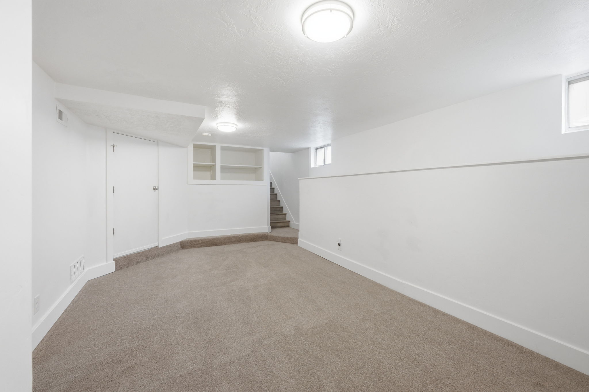 Carpeted room featuring a neutral color palette, integrated ceiling lighting, built-in shelving, and white baseboards