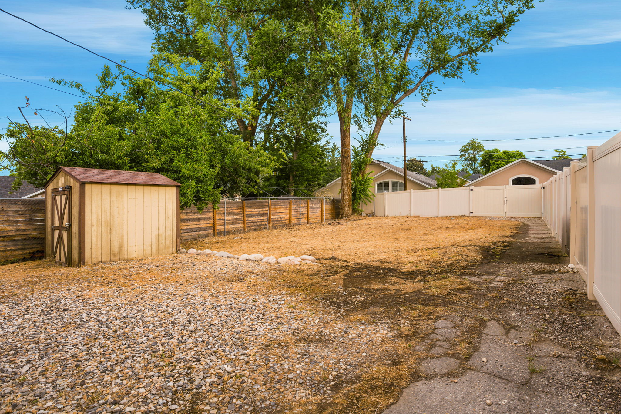Expansive yard featuring a gravel area, a detached storage shed with a shingled roof, a vinyl fence, and a wooden fence