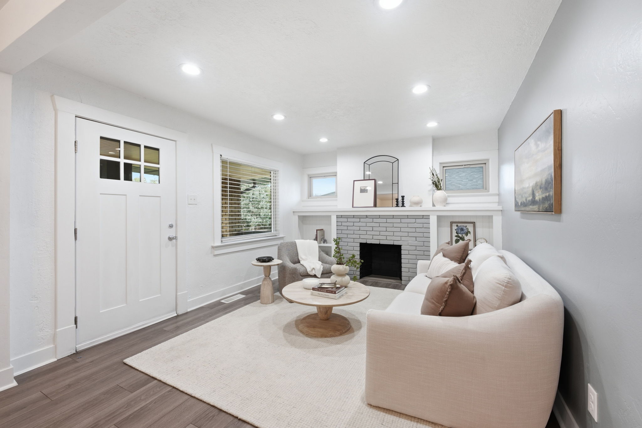 Living area featuring wood-finish flooring, a white paneled entry door with glass inserts, recessed lighting, and a painted brick fireplace with a white mantel and built-in shelving