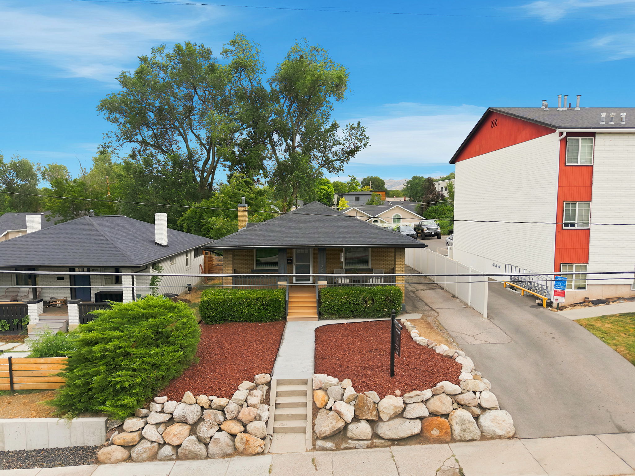 Single-story residence featuring a dark shingled roof, a covered porch with white railing, and a concrete walkway