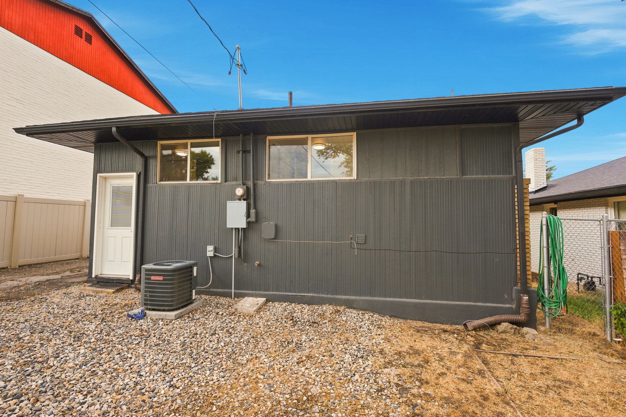 Rear exterior featuring dark vertical siding, a white service door, and two windows