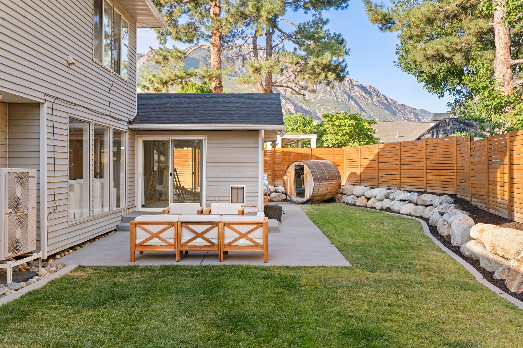 Spacious backyard featuring a concrete patio, verdant lawn, a horizontal slat privacy fence, and a unique barrel sauna
