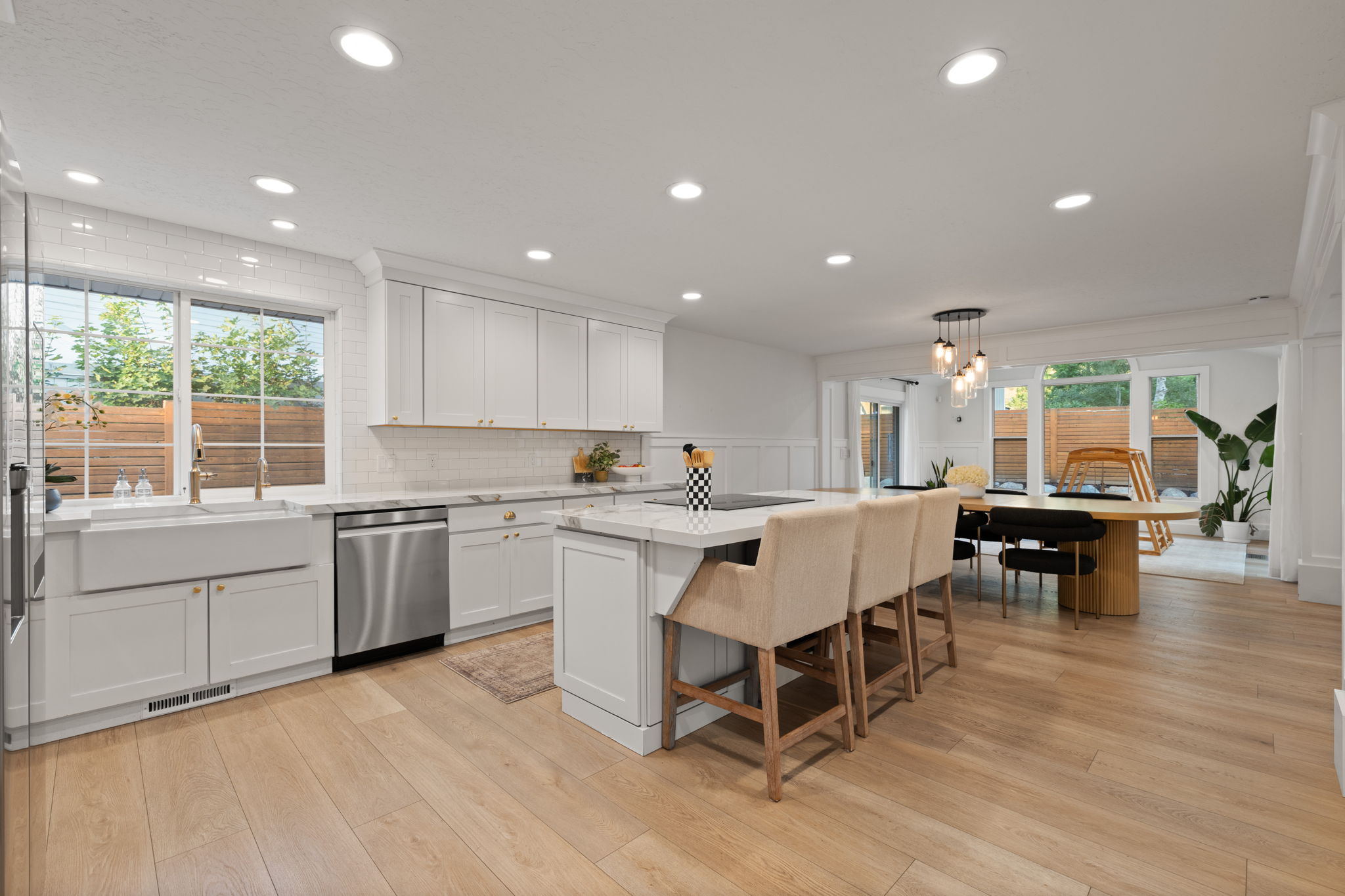 Spacious kitchen featuring light wood-finish flooring, white cabinetry, a large kitchen island with seating, a farmhouse sink, and stainless steel appliances