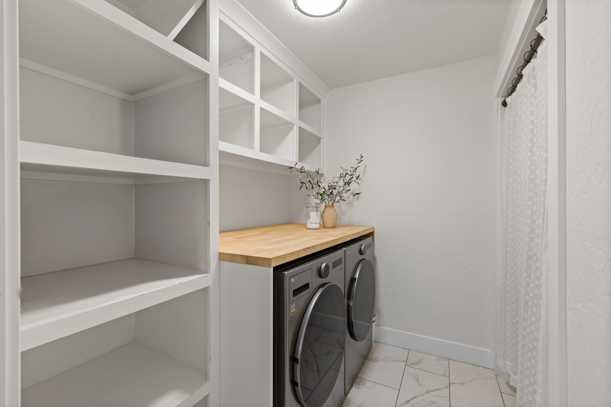 Laundry area featuring built-in white shelving, wood-finish countertop, and tile flooring