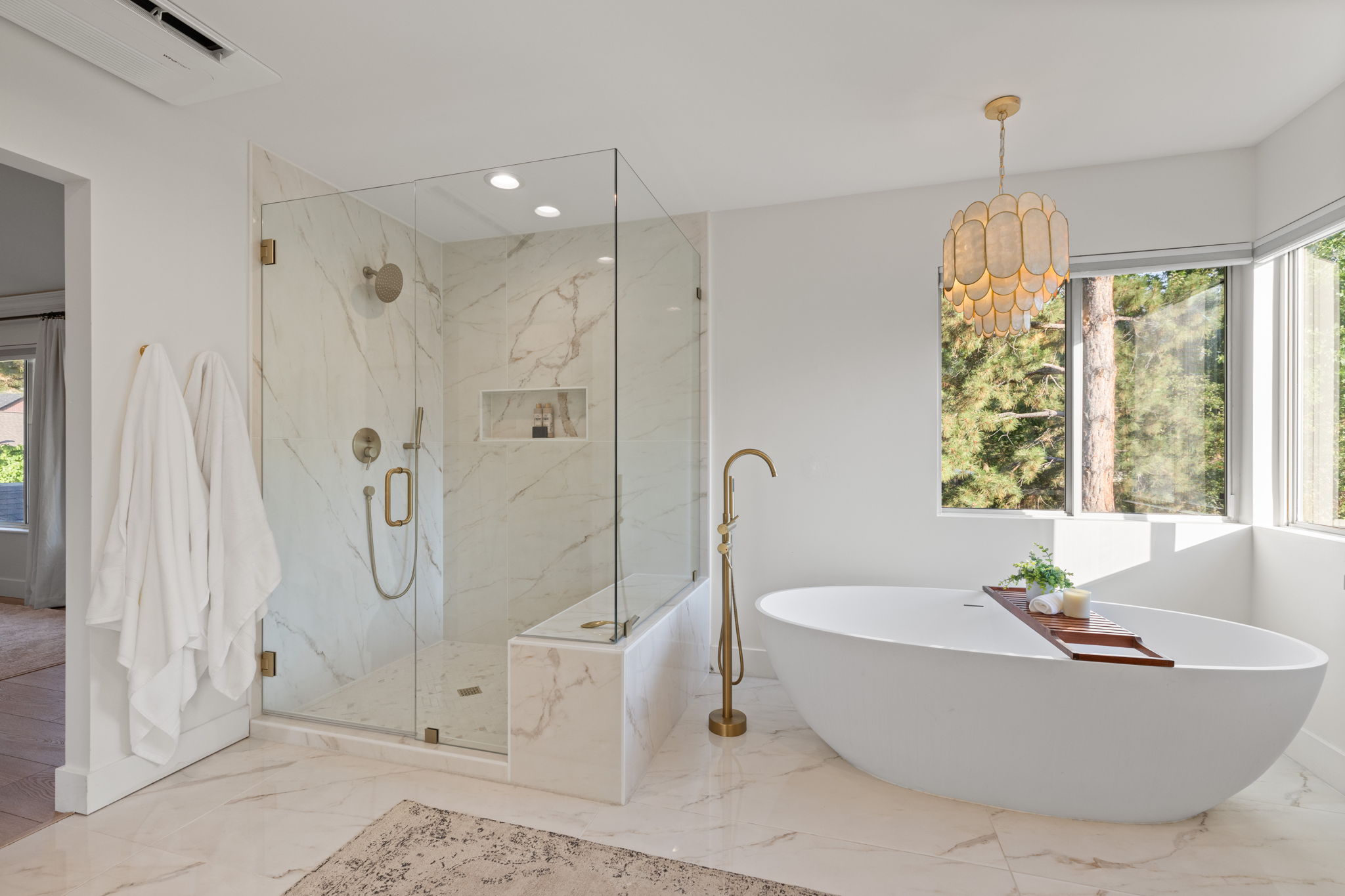 Spacious bathroom featuring a freestanding soaking tub with a floor-mounted faucet, a walk-in shower with a glass enclosure and built-in bench, and large format marble-look floor and wall tiling