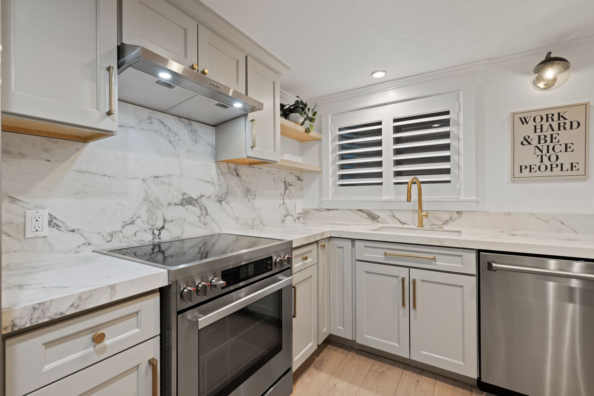 Modern kitchen featuring light gray cabinetry with brass hardware, a built-in stainless steel range, and a matching dishwasher