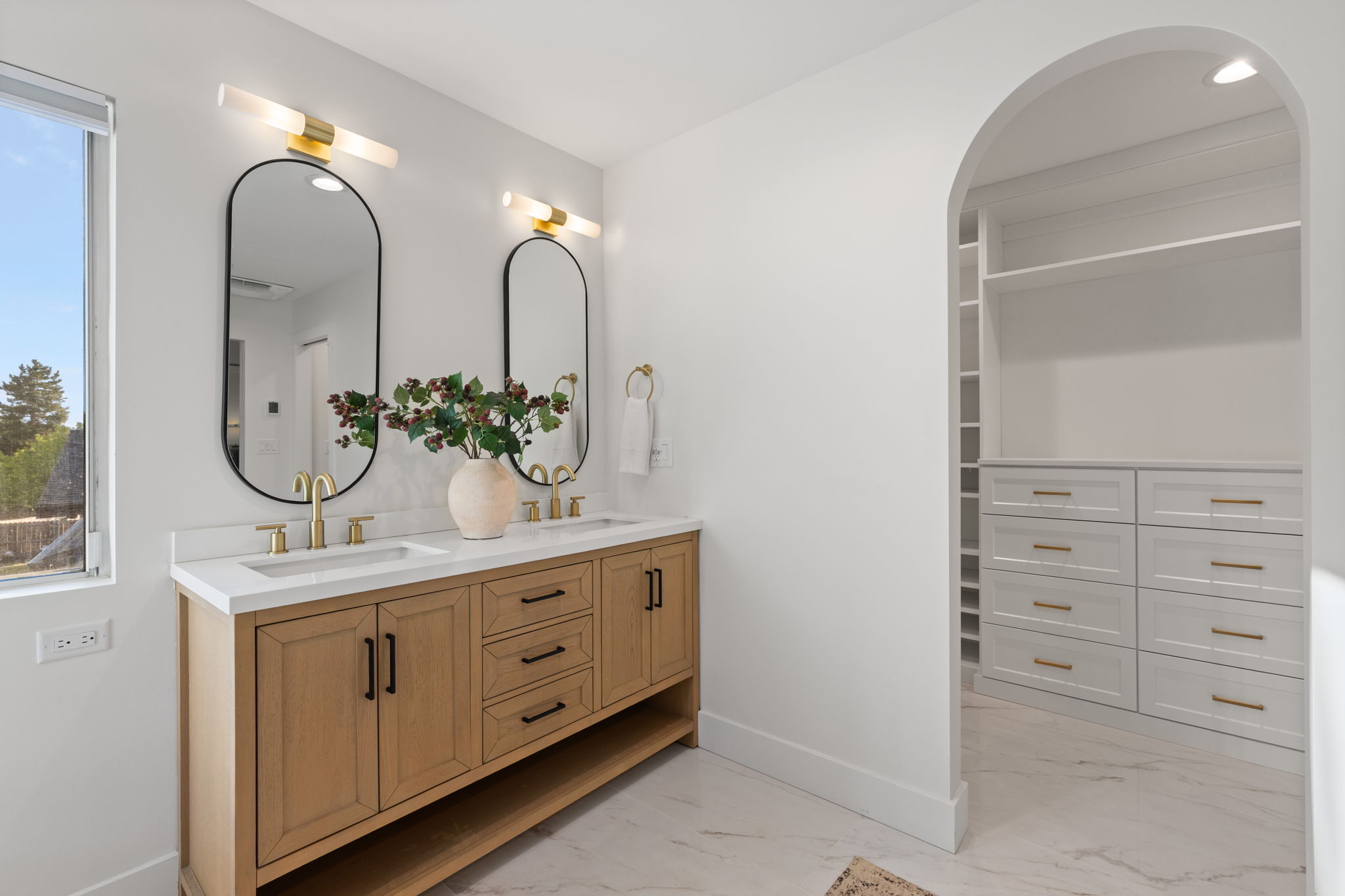 Dual vanity with light wood-finish cabinetry, white countertop, and gold-finish fixtures