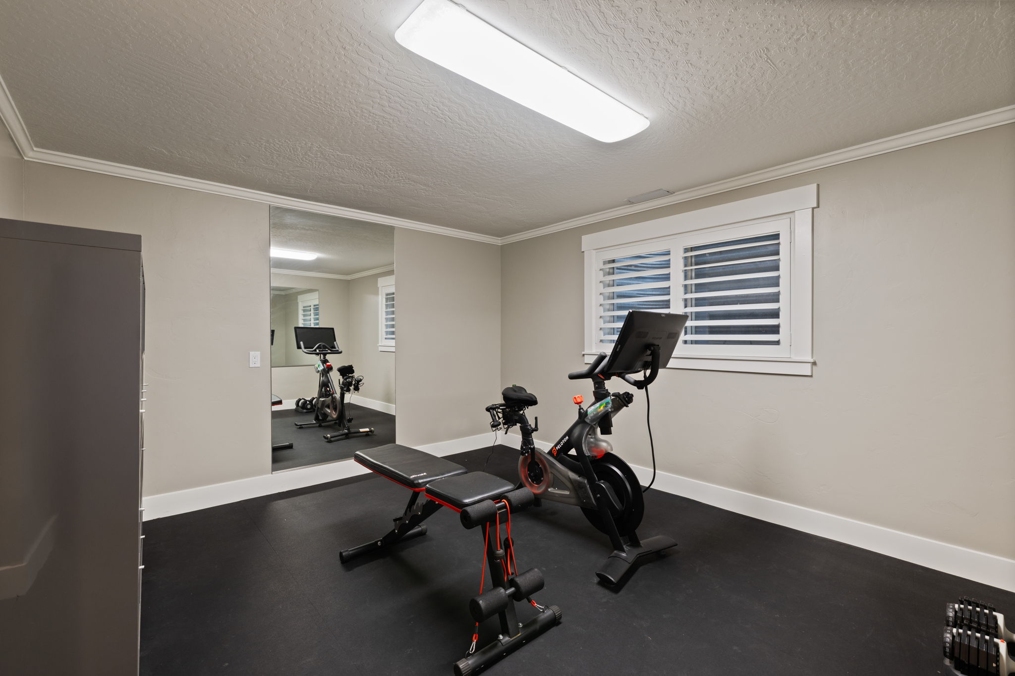 Dedicated fitness area featuring durable black rubber flooring, a large mirrored wall, a window with white plantation shutters, crown molding, and recessed lighting