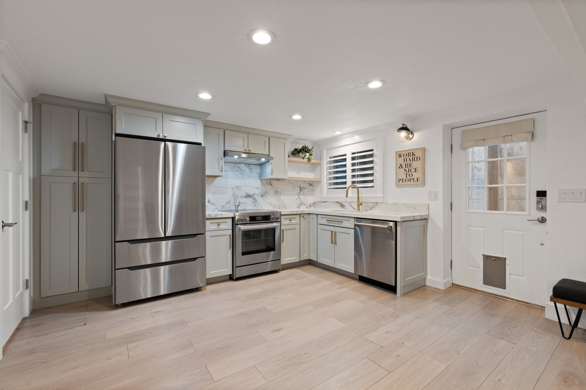 L-shaped kitchen featuring wood-finish flooring, light gray cabinetry, stainless steel appliances, and a marble backsplash