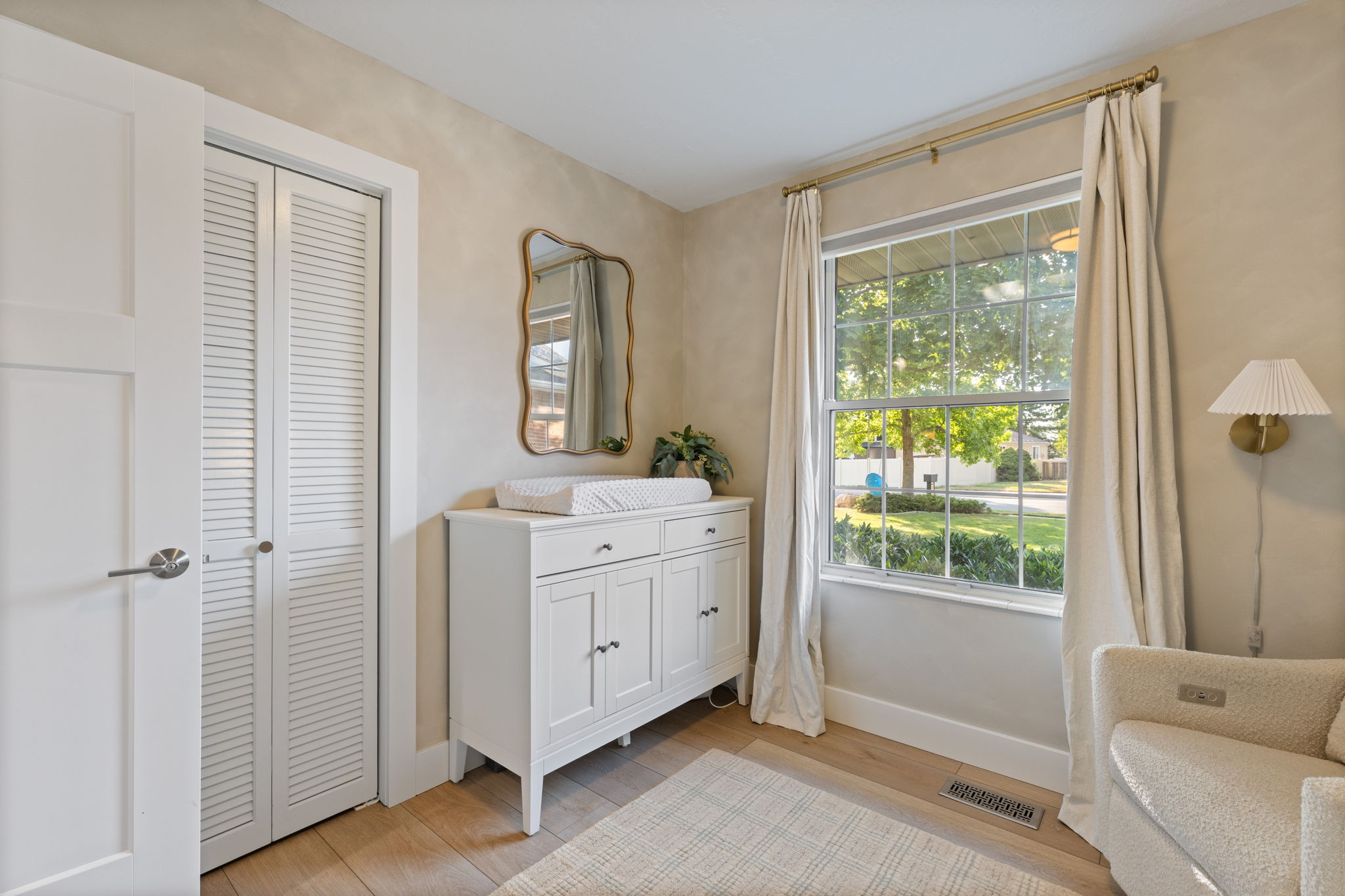 Room featuring wood-finish flooring, a double-paned window with exterior views, white louvered bifold closet doors, a white four-panel interior door, and a decorative wall sconce