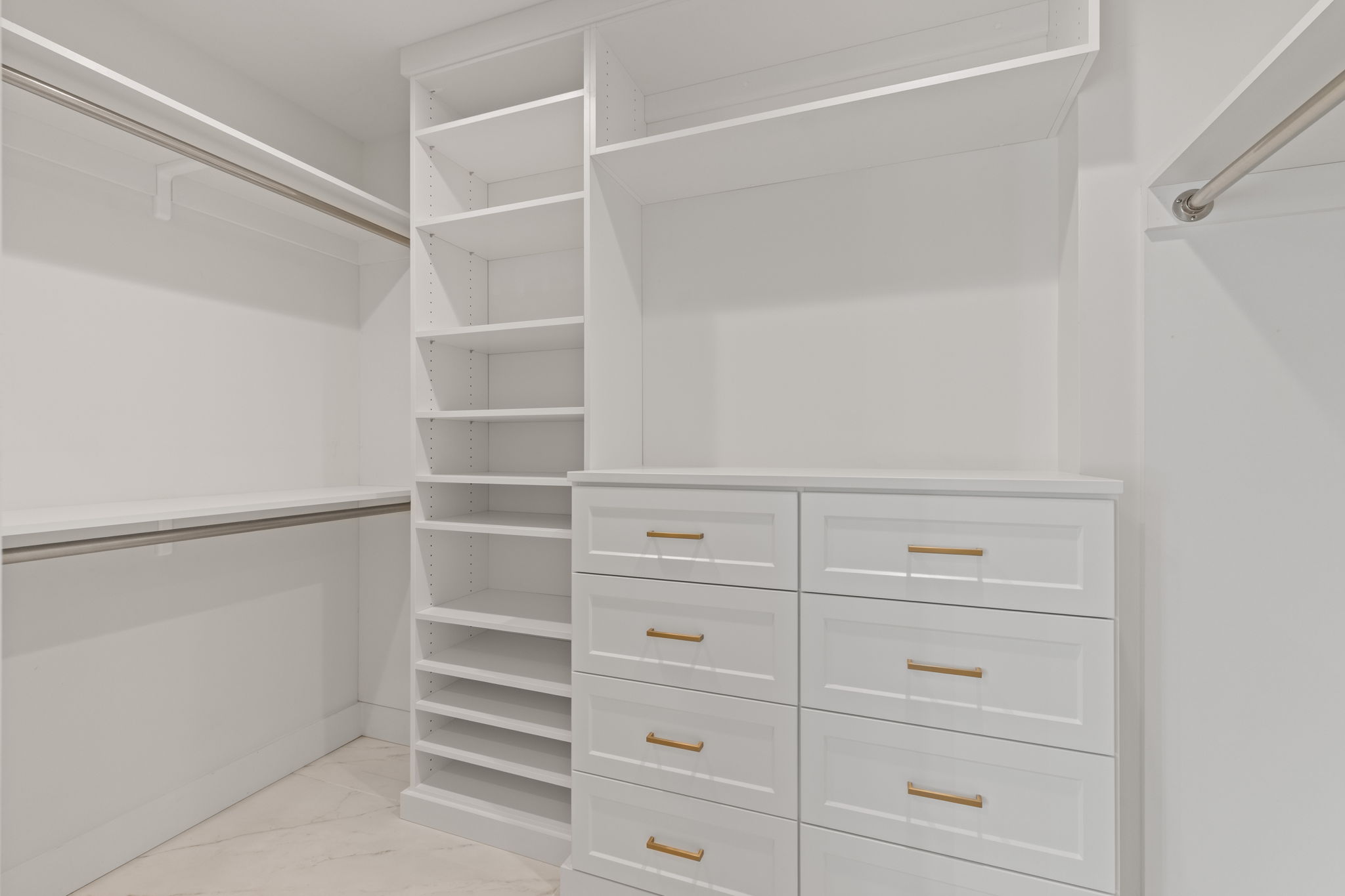 Custom-designed closet system featuring white cabinetry, built-in shelving, multiple drawers with gold-finish hardware, and hanging rods