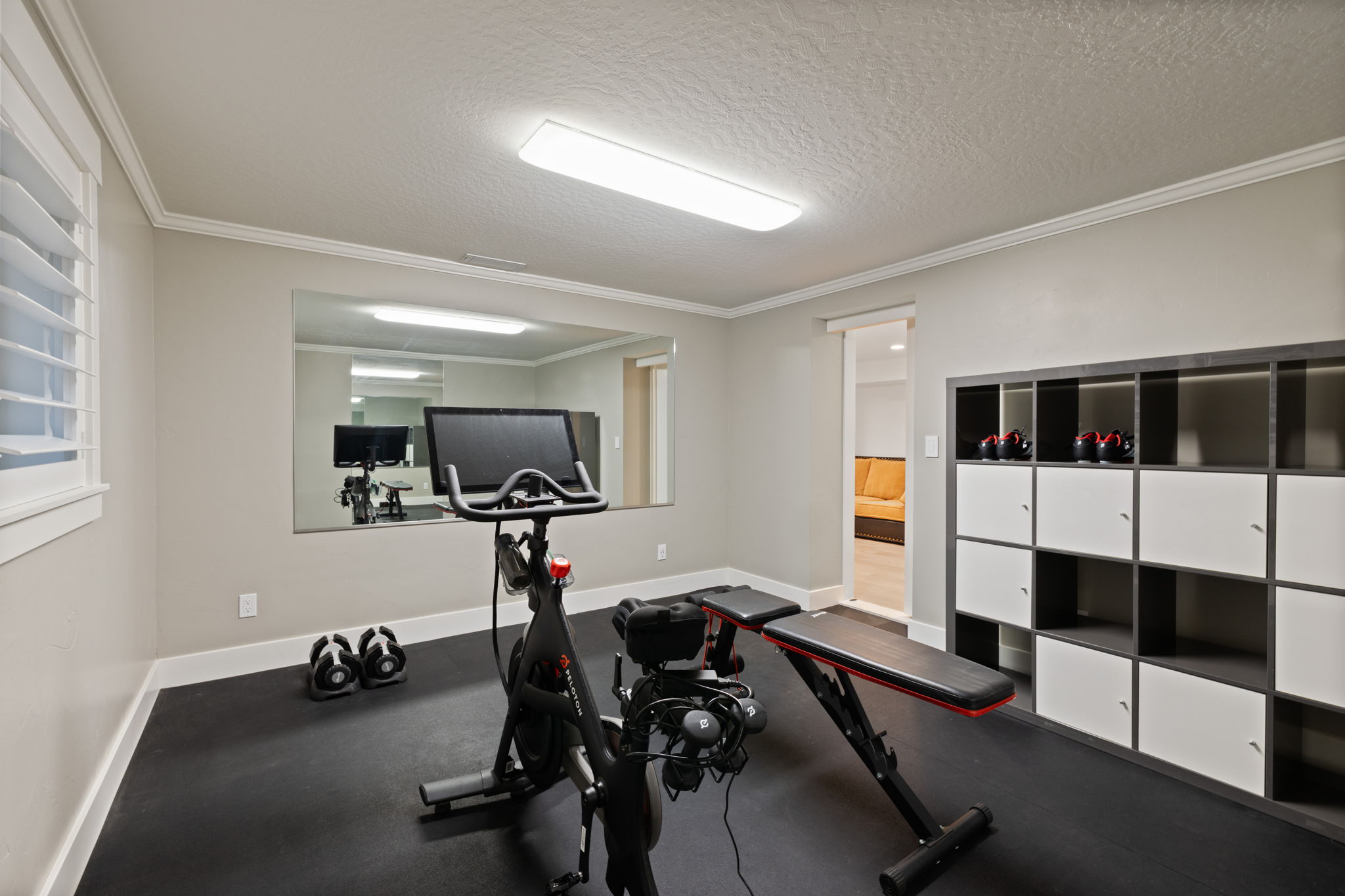 Dedicated exercise room featuring a full-wall mirror, plantation shutters, and rubber flooring