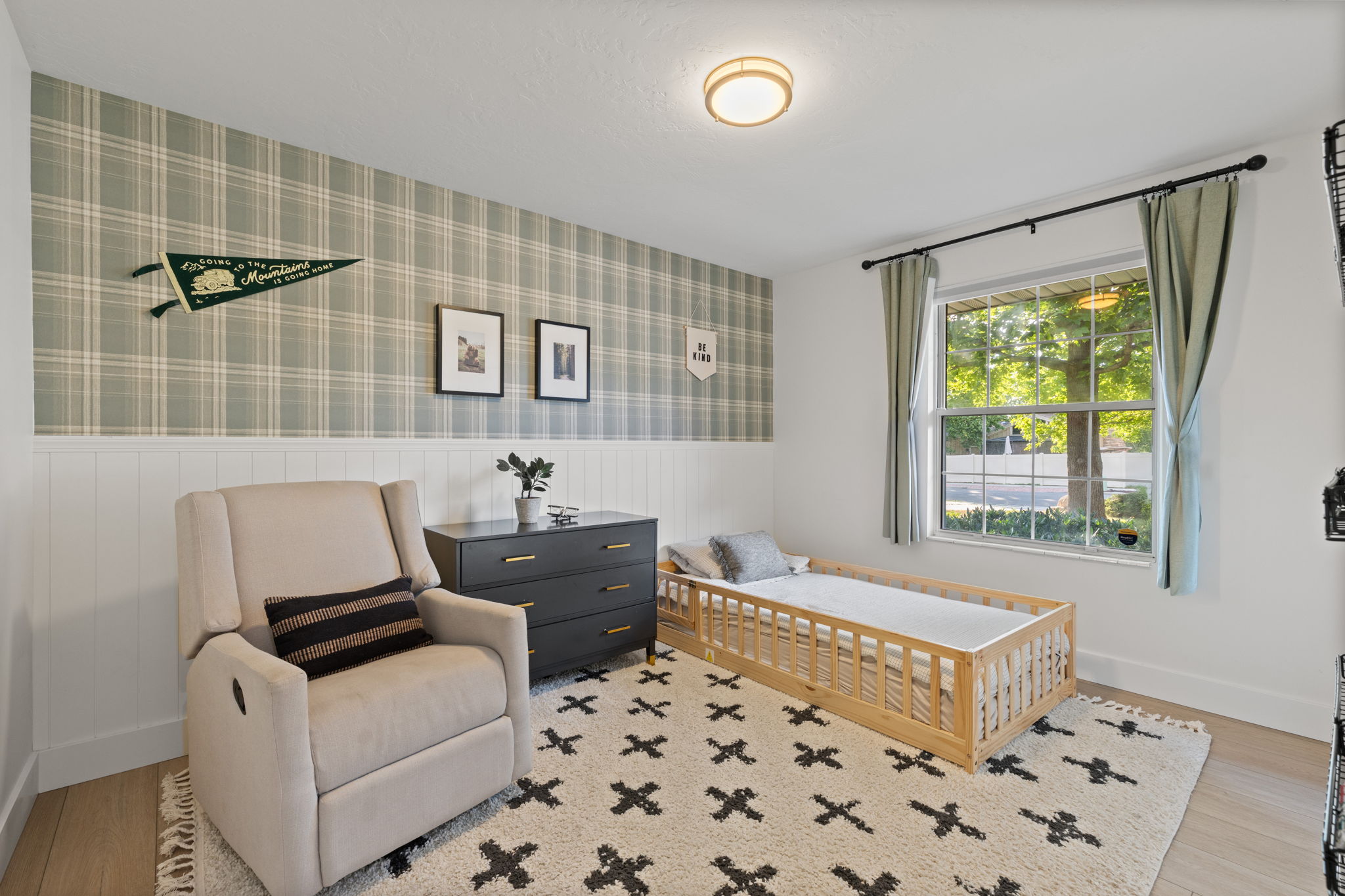 Room featuring a large window, a wall with plaid wallpaper above white wainscoting, and wood-finish flooring