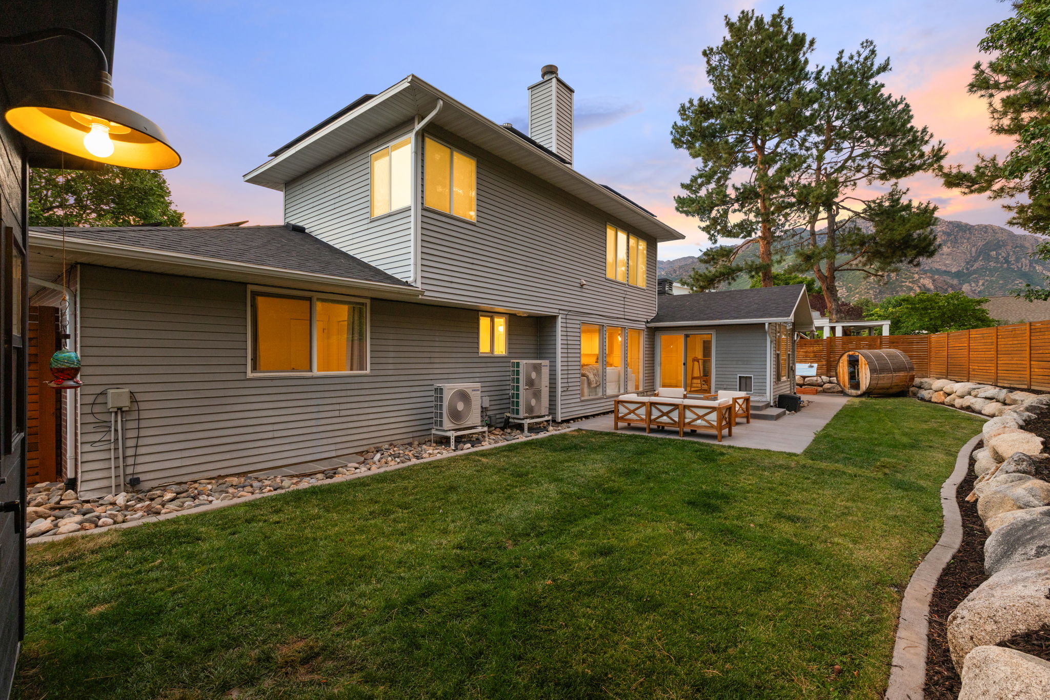 Expansive backyard featuring a manicured lawn, concrete patio, and a retaining wall with rock landscaping