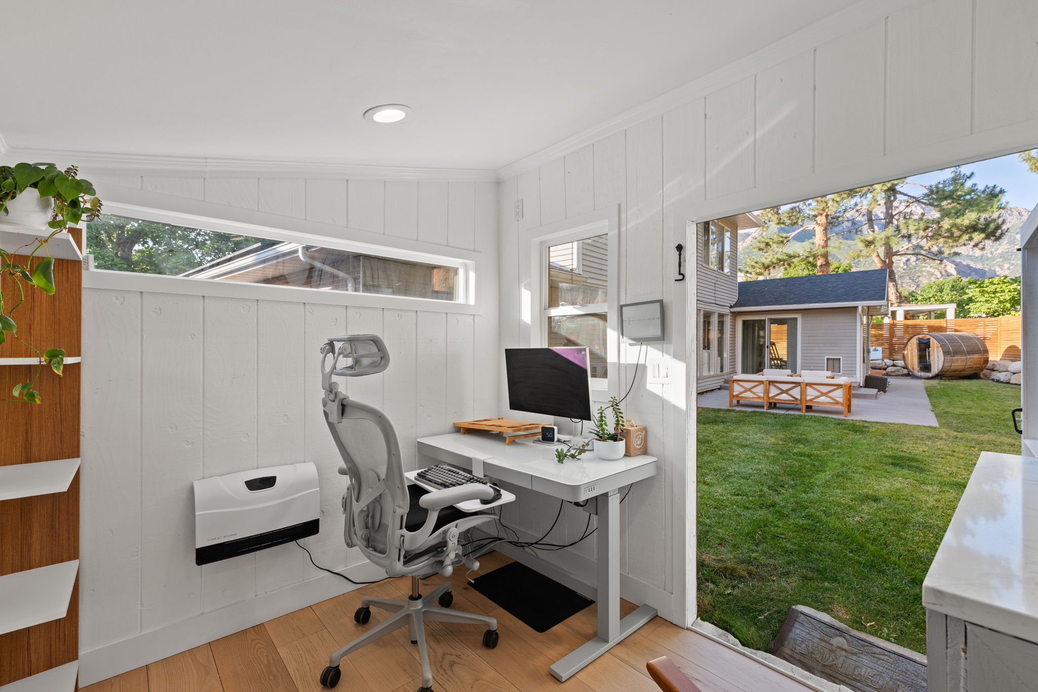 Light-filled ancillary structure featuring wood-finish flooring, white shiplap walls, a horizontal transom window, and a wall-mounted heating unit