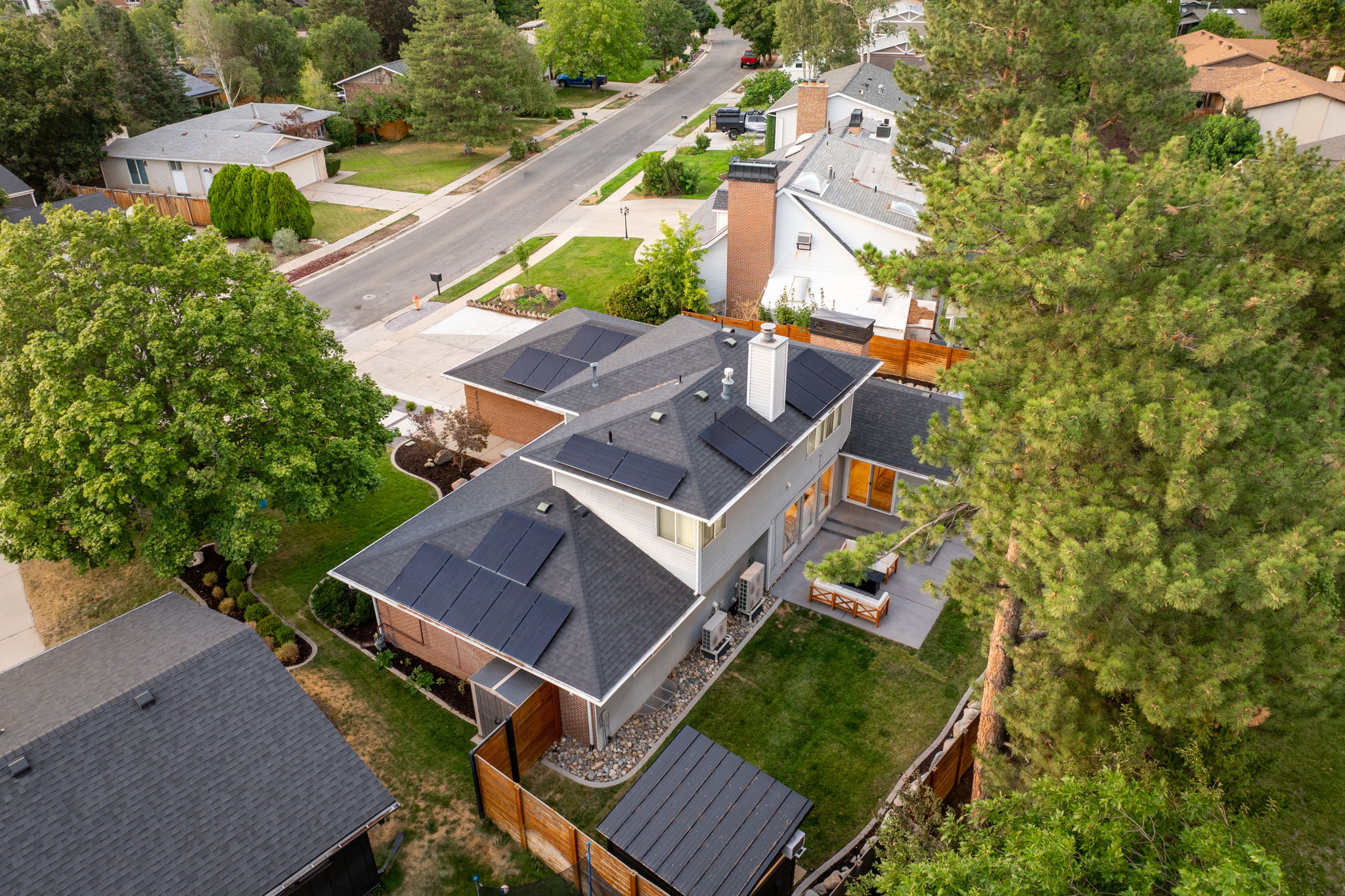 Contemporary residence featuring a multi-level roofline with integrated solar panels, a paved patio, and a landscaped backyard with mature trees
