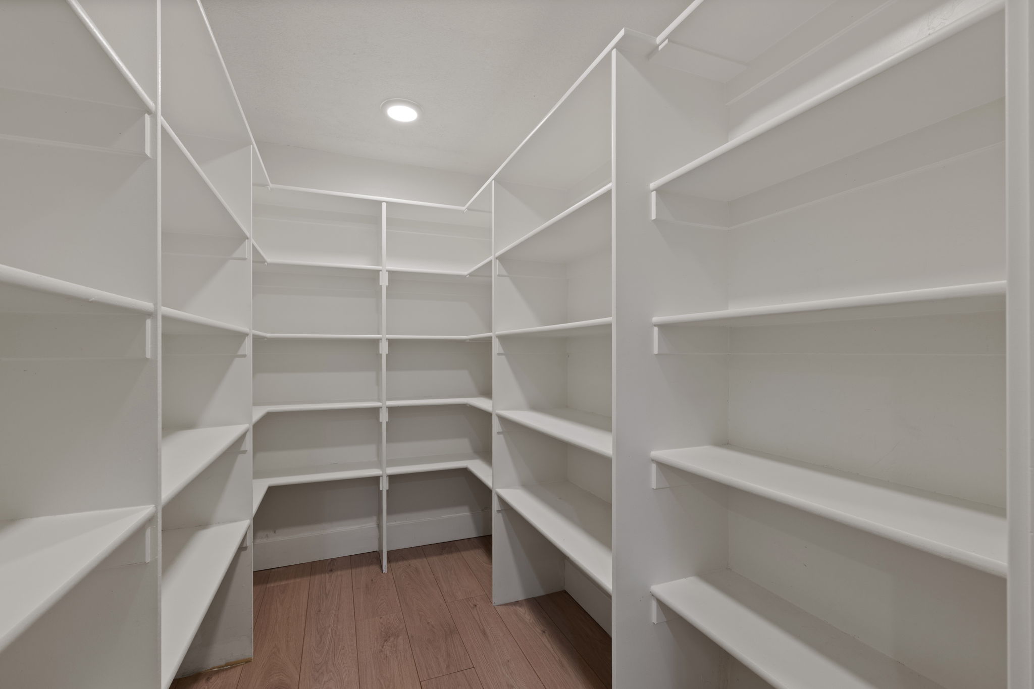Spacious walk-in pantry with extensive built-in shelving, wood-finish flooring, and recessed ceiling lighting