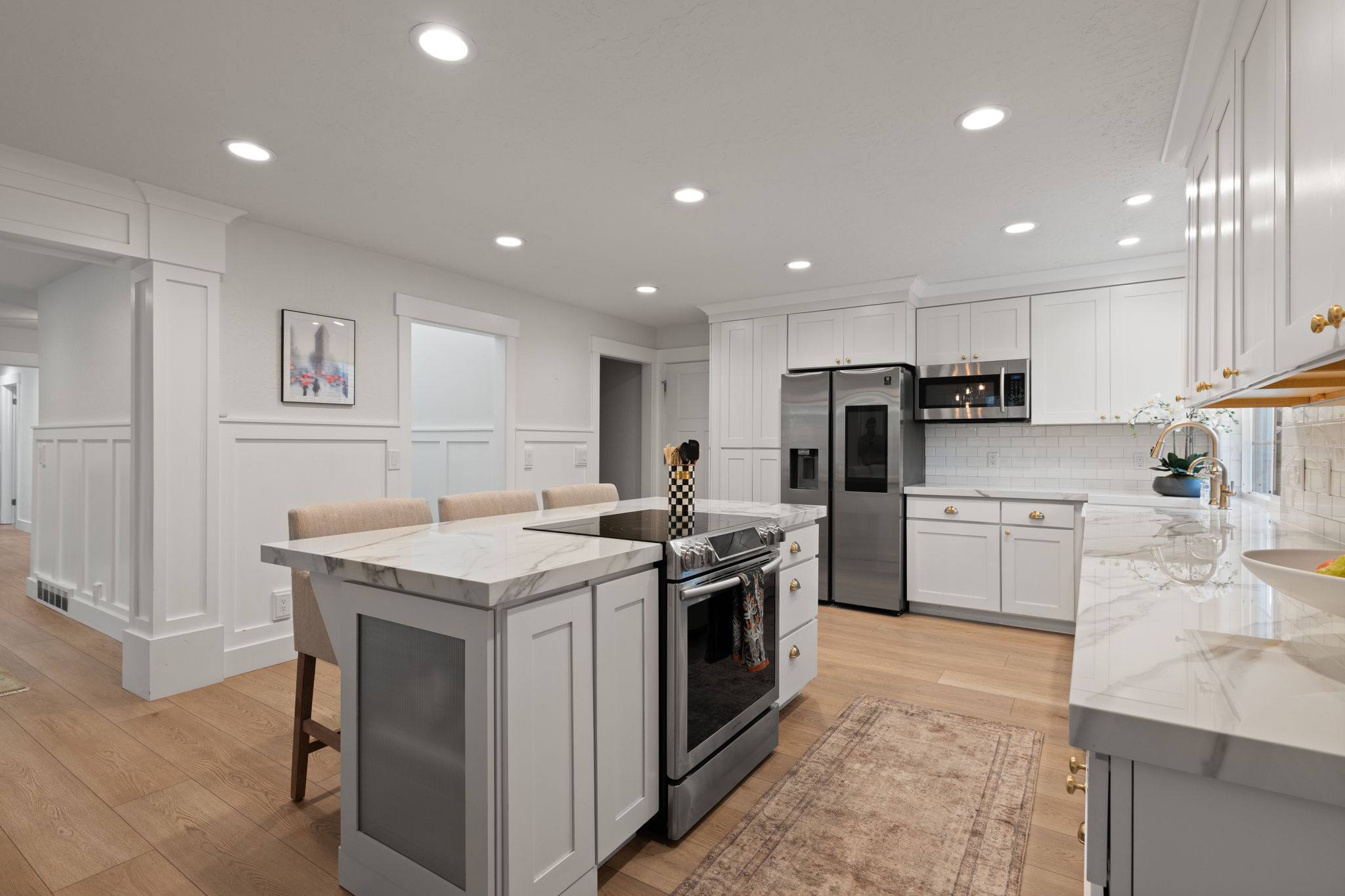 Kitchen featuring light wood-finish flooring, white cabinetry, integrated stainless steel appliances, a center island with a built-in cooktop, and recessed lighting