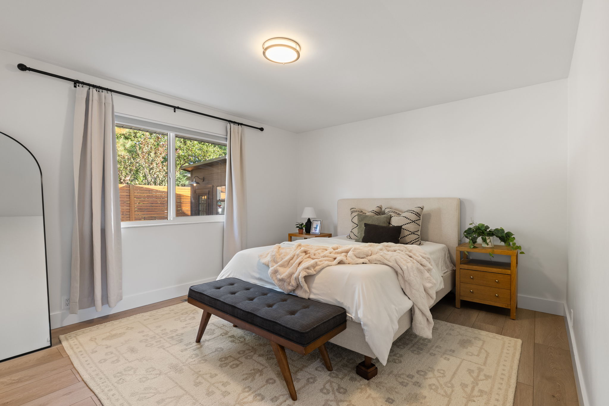 Light-filled bedroom featuring wood-finish flooring, a contemporary ceiling light fixture, and a large window