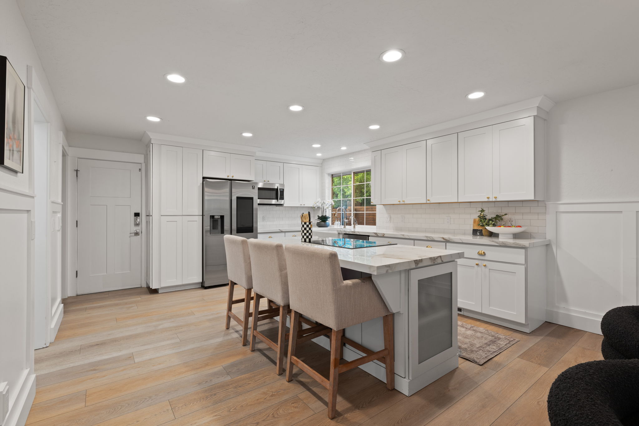 Contemporary kitchen featuring a substantial island with integrated cooktop, white cabinetry, integrated stainless steel appliances, marble-look countertops, and wood-finish flooring