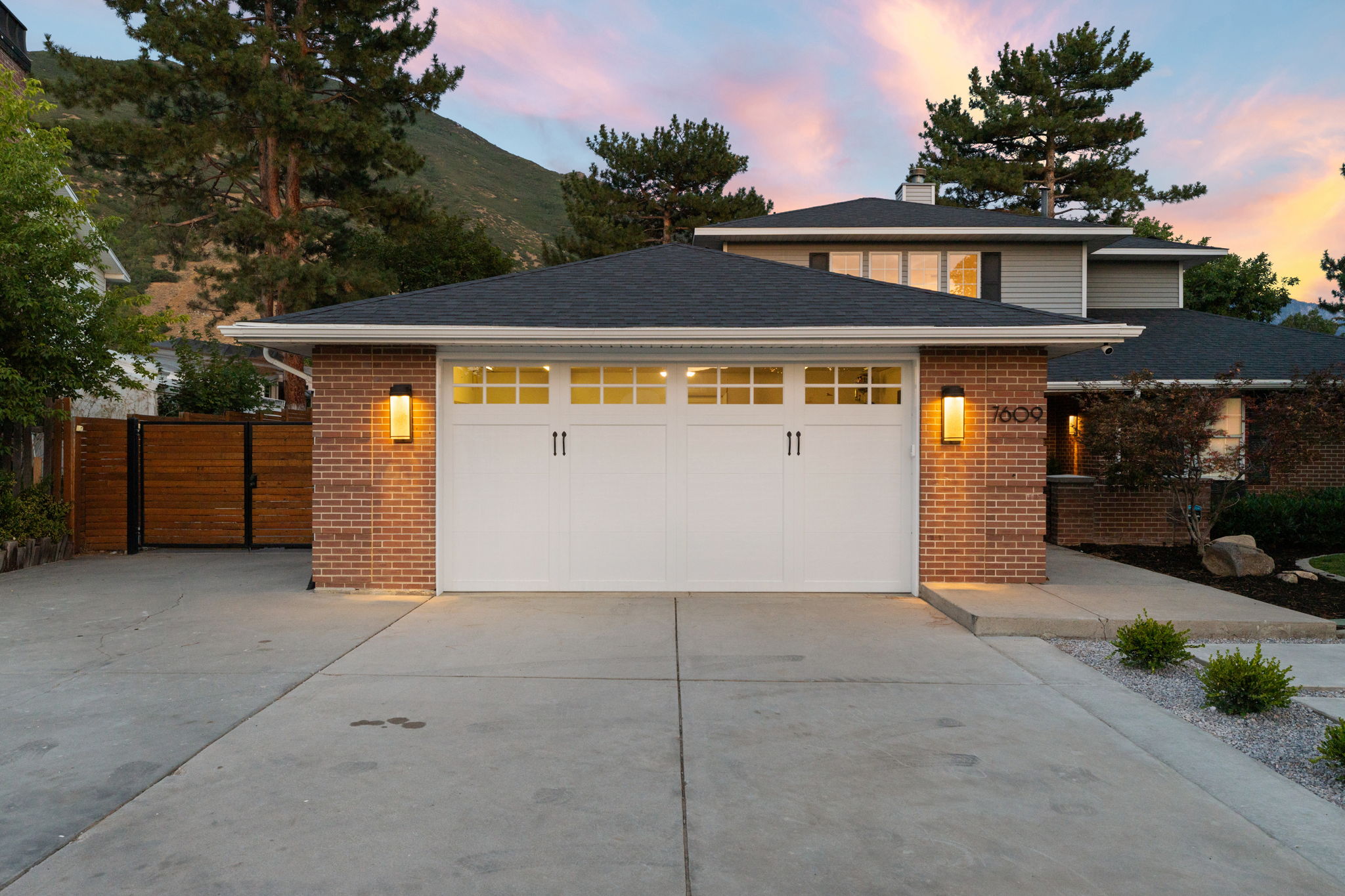 Brick facade home featuring a two-car garage with transom windows, a concrete driveway, and a dark shingle roof