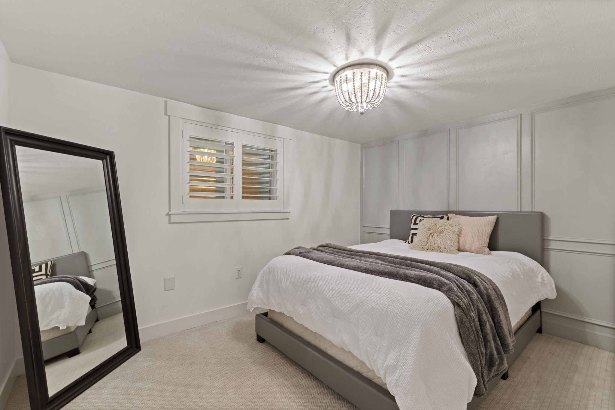 Bedroom featuring white plantation shutters, a decorative ceiling light fixture, panel molding on walls, and light-colored carpeting