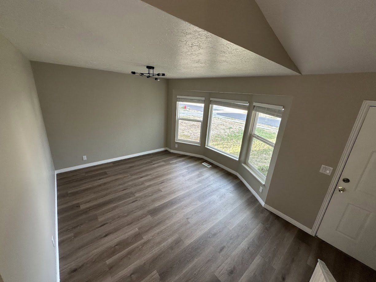Spacious room with wood-finish flooring, a modern multi-bulb ceiling fixture, and a bay window