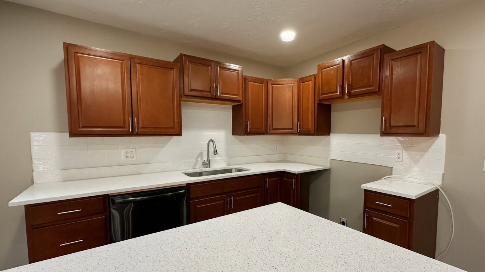 Kitchen featuring rich wood-finish cabinetry, white speckled countertops, a subway tile backsplash, and a stainless steel sink with a gooseneck faucet