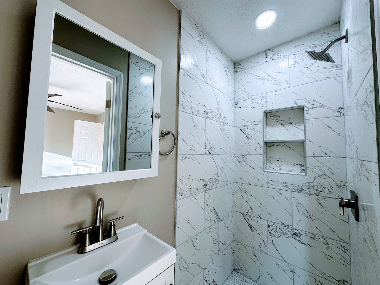 Shower enclosure featuring white marble-look subway tile with dual recessed niches and a dark-finish rain shower head