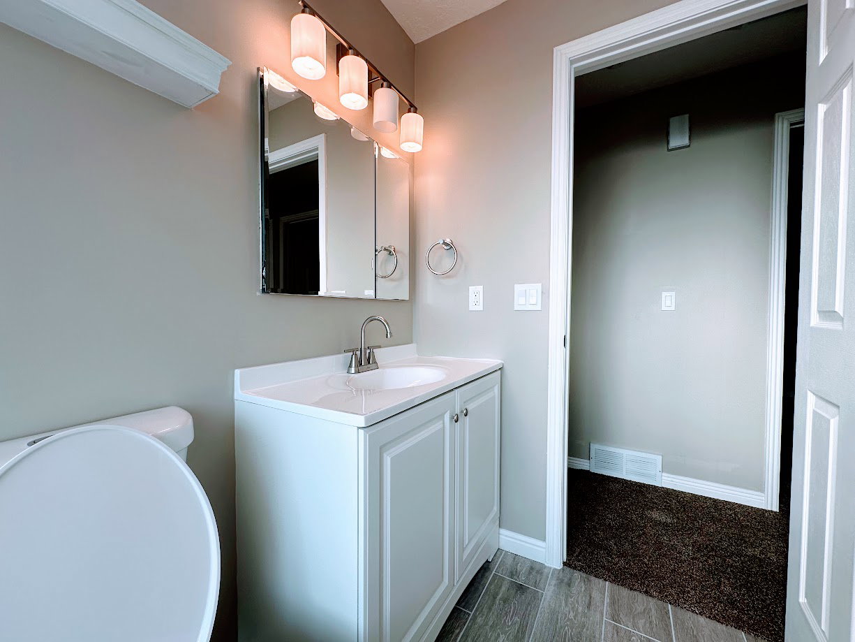 Bathroom featuring a white vanity with paneling, an integrated sink, and brushed nickel fixtures