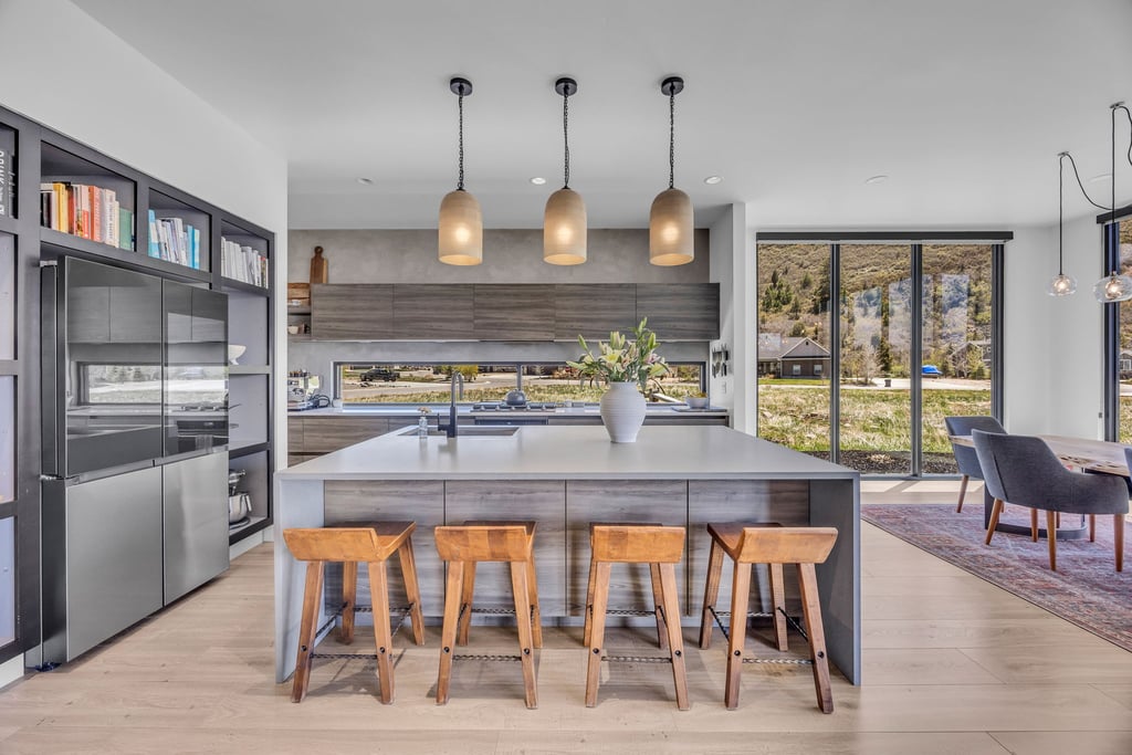 Modern kitchen featuring an expansive island with seating, pendant lighting, built-in shelving, integrated refrigerator, and large windows