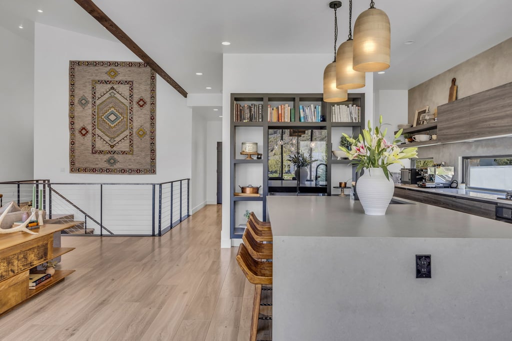 Open-concept living area featuring wood-finish flooring, a contemporary kitchen island with a light-toned countertop, built-in shelving, vaulted ceilings, and a cable railing system