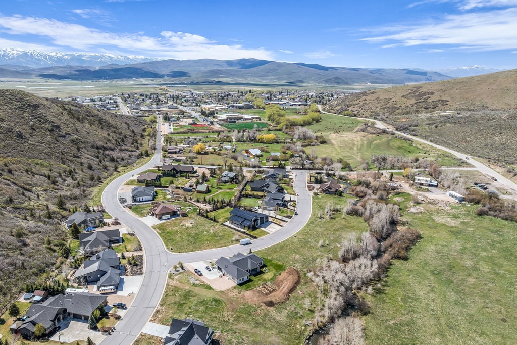 Aerial perspective showcasing a residential development with winding paved roads, surrounded by lush green fields and natural terrain
