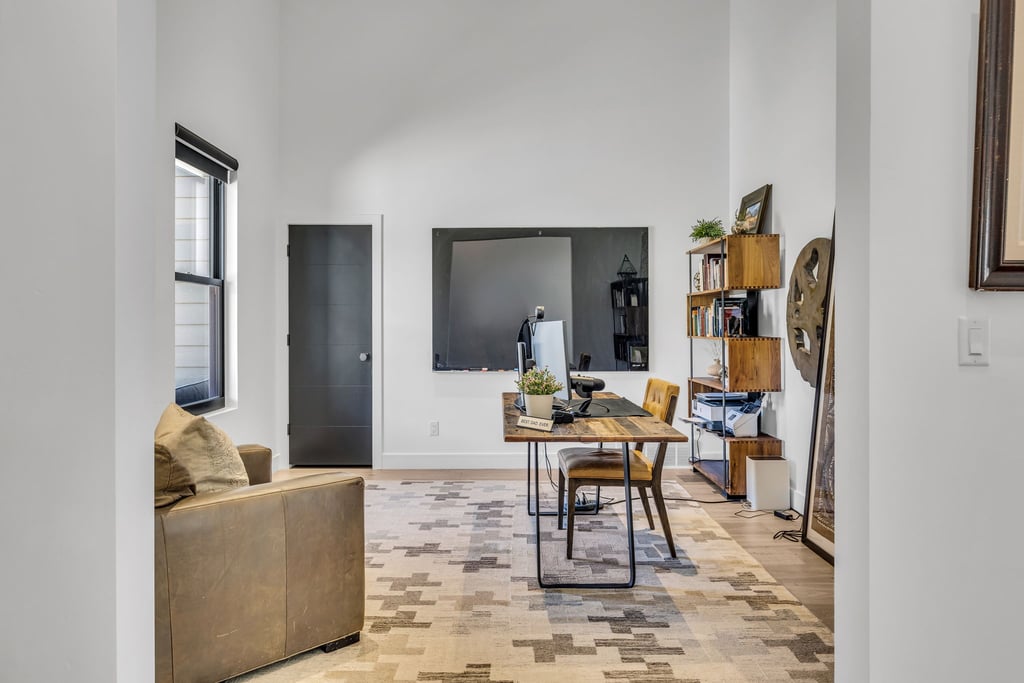 Open-concept room featuring wood-finish flooring, a contemporary black door, and a tall window with roller shade
