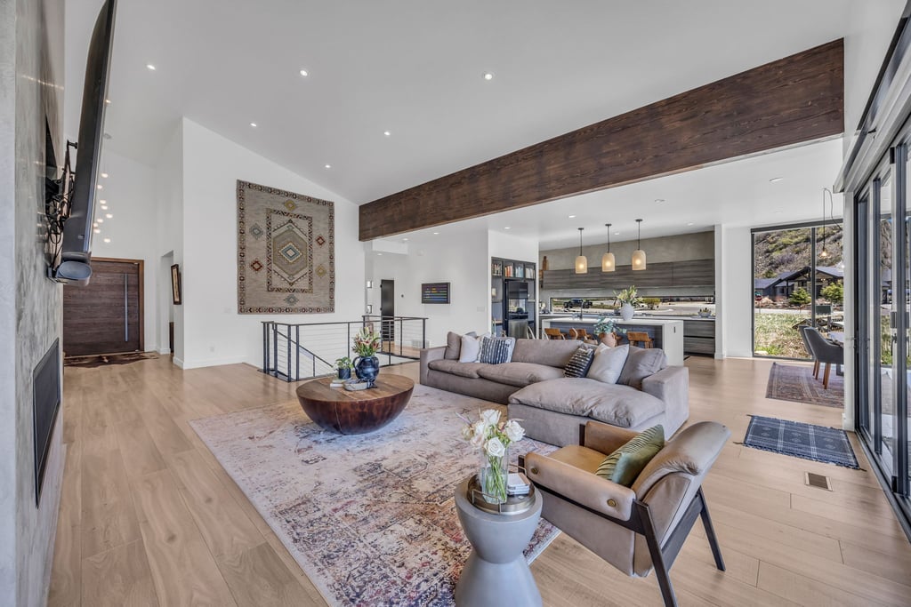Open-concept living area with vaulted ceilings, light wood-finish flooring, and a prominent wood beam detail