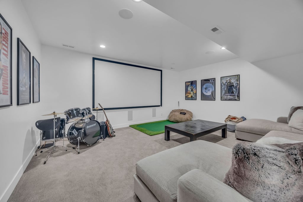 Spacious entertainment room featuring a large projection screen, recessed ceiling lighting, and light-toned carpet flooring
