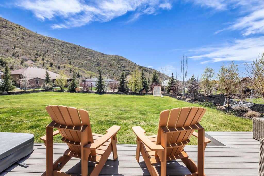 Expansive backyard featuring a manicured lawn, tiered landscaping, mature trees, and a mountain backdrop